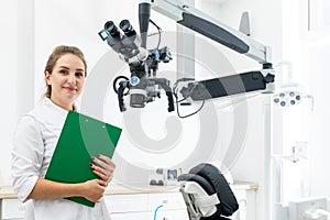 Smiling female dentist holding clipboard with patient records in hands at dental clinic with copy space