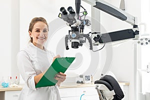 Smiling female dentist holding clipboard with patient records in hands at dental clinic with copy space