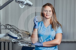 Smiling female dentist holding dental mirror while standing in her dentist office.