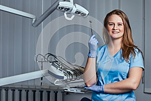 Smiling female dentist holding dental mirror while standing in her dentist office.
