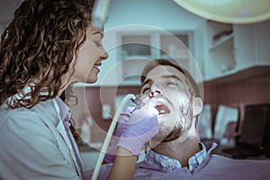 Smiling female dentist operate young man.