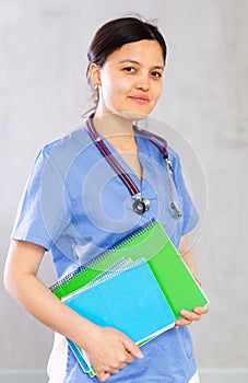 Smiling female doctor in blue uniform standing with notebooks