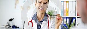 Smiling female doctor with glasses and stethoscope communicates with colleague with tablet in hand in clinic