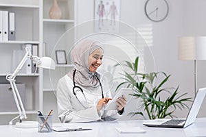 Smiling female doctor in hijab using tablet in office