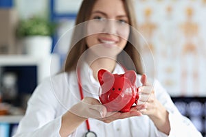 Smiling female doctor holding red pig piggy bank