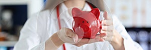 Smiling female doctor holding red pig piggy bank