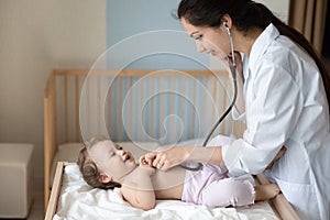 Smiling female doctor pediatrician using stethoscope, checking little girl lungs