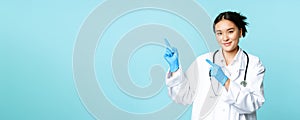 Smiling female doctor, physican in medical uniform and sterile gloves, pointing fingers left at promo, clinic logo