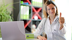 Smiling female doctor posing in clinic office and showing thumb up gesture