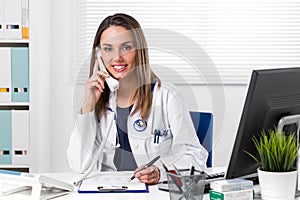 Smiling female Doctor sat at desk with telephone to ear