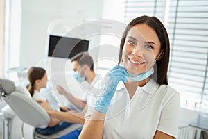 Smiling female doctor showing looking at the camera while her collegue working with girl in dental chair on the background