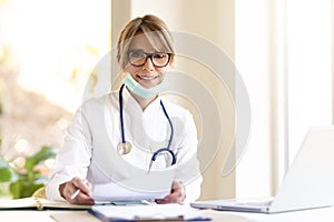 Smiling female doctor sitting at desk in doctor`s office and working photo