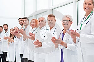 Smiling female doctor standing in front of her applauding colleagues.