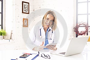 Smiling female doctor using digital tablet and laptop while working in doctor`s office photo