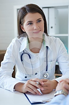 Smiling female doctor wearing coat attending to her patient in a consultation while is holding a medical history sitting