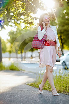 smiling female in dress and jacket in city talking on phone