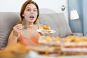 smiling female eating sweet cake on sofa