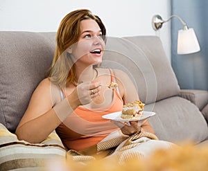smiling female eating sweet cake on sofa