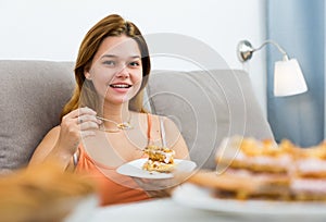 smiling female eating sweet cake on sofa