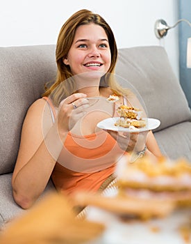 smiling female eating sweet cake on sofa
