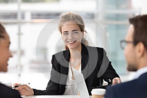 Smiling female employee listen to colleague discussion at meeting