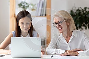 Smiling female employees work on laptop in office
