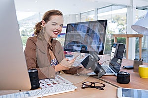 Smiling female executive using mobile phone while holding digital camera in office