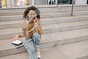 Smiling female freelancer talking phone with client while sitting on building background