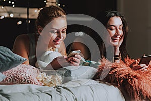 Smiling female friends engaged by their smartphones