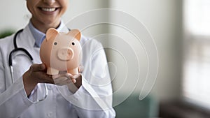 Smiling female GP doctor holding piggy bank on hands