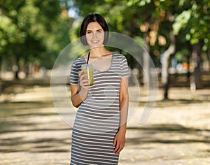 Smiling female with a green smoothie. Healthy women on a blurred park background. Healthy lifestyle concept. Copy space.