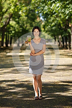 Smiling female with a green smoothie. Healthy women on a blurred park background. Healthy lifestyle concept. Copy space.