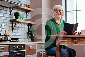 Smiling female happily keeping book in hands at kitchen room