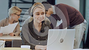 Smiling female helpline operator with headphones at her desk in the office