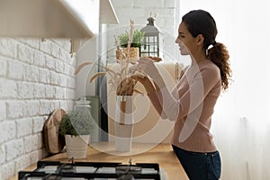 Smiling female homeowner improving dwelling with dried flowers.