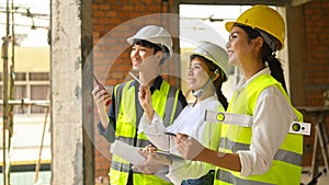 Smiling female investor and engineer managers wearing safety helmet working, checking plan together at construction site