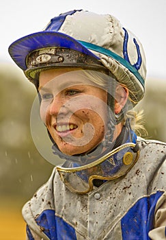 Smiling female jockey with a muddy face in the rain