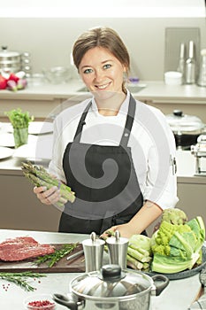 Smiling female kitchener in uniform is standing in the kitchen at the restaurant