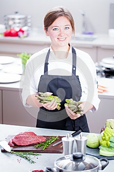 Smiling female kitchener in uniform is standing in the kitchen at the restaurant