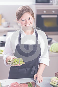 Smiling female kitchener in uniform is standing in the kitchen at the restaurant