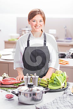 Smiling female kitchener in uniform is standing in the kitchen at the restaurant