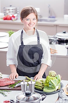 Smiling female kitchener in uniform is standing in the kitchen at the restaurant