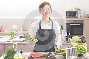 Smiling female kitchener in uniform is standing in the kitchen at the restaurant