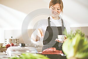 Smiling female kitchener in uniform is standing in the kitchen at the restaurant