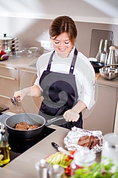 Smiling female kitchener in uniform is standing in the kitchen at the restaurant