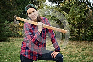 Smiling female lumberjack holding a huge axe on her shoulder