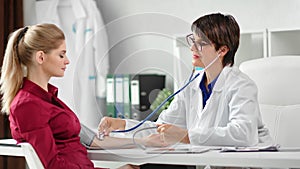 Smiling female medical worker measuring pressure to girl patient at white room clinic interior