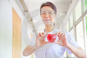 Smiling female nurse holding red smile heart in her hands. Red heart Shape representing high quality service mind to patient.