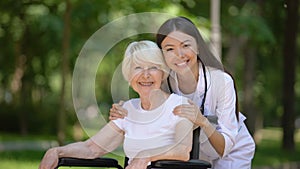 Smiling female nurse hugging disabled elderly woman and looking at camera