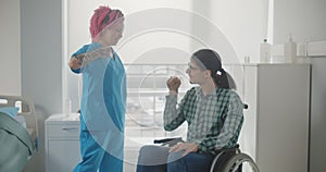 Smiling female nurse and male patient in wheelchair sharing secret hand gesture